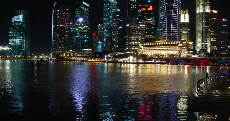 The Marina Bay waterfront at night, with lit office towers and the Fullerton Hotel across the water