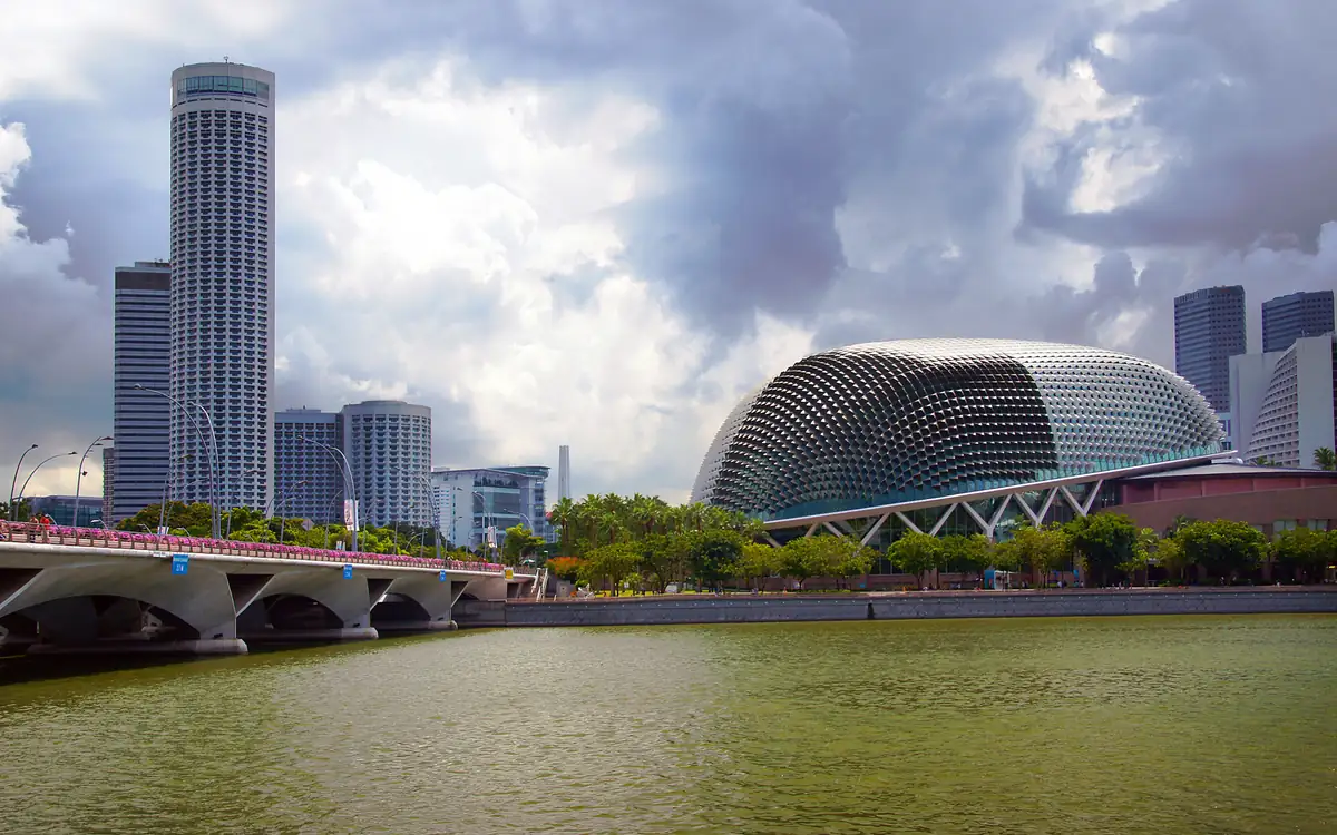 The Esplanade, Theatres on the Bay, beside the river under a broken cloudy sky, with a bridge and city towers at left