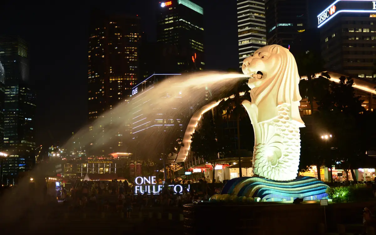 The Merlion statue at Merlion Park at night, with its water jet and the city lights behind it