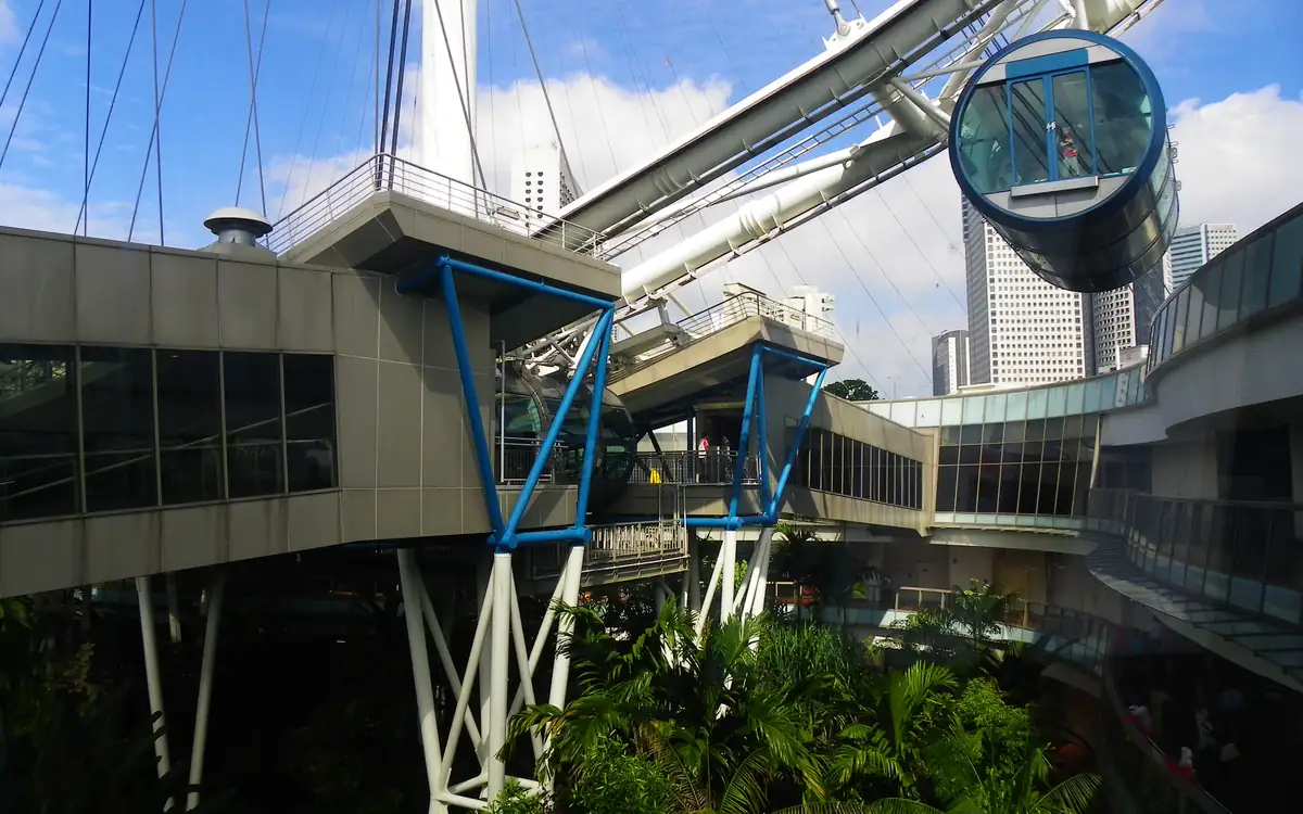 The Singapore Flyer’s passenger capsule and support structure beside a glass-walled walkway, with trees below