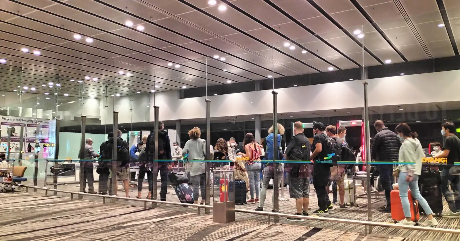Changi Airport Terminal 3 security queue, with travellers in line beside glass screens and overhead lighting