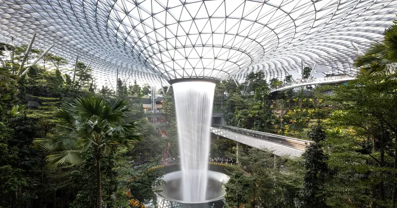 The Jewel Changi Airport Rain Vortex waterfall, falling through a glass-roofed atrium lined with tropical trees