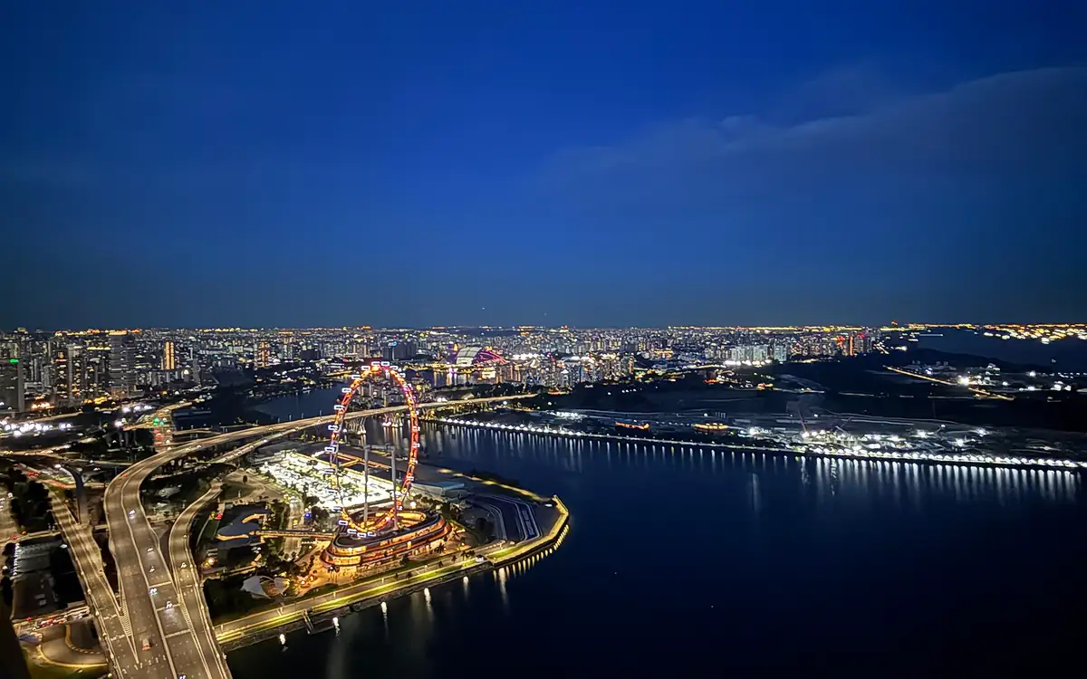 The Marina Bay waterfront at dusk, seen from above, with the Singapore Flyer lit beside the bay and the city beyond