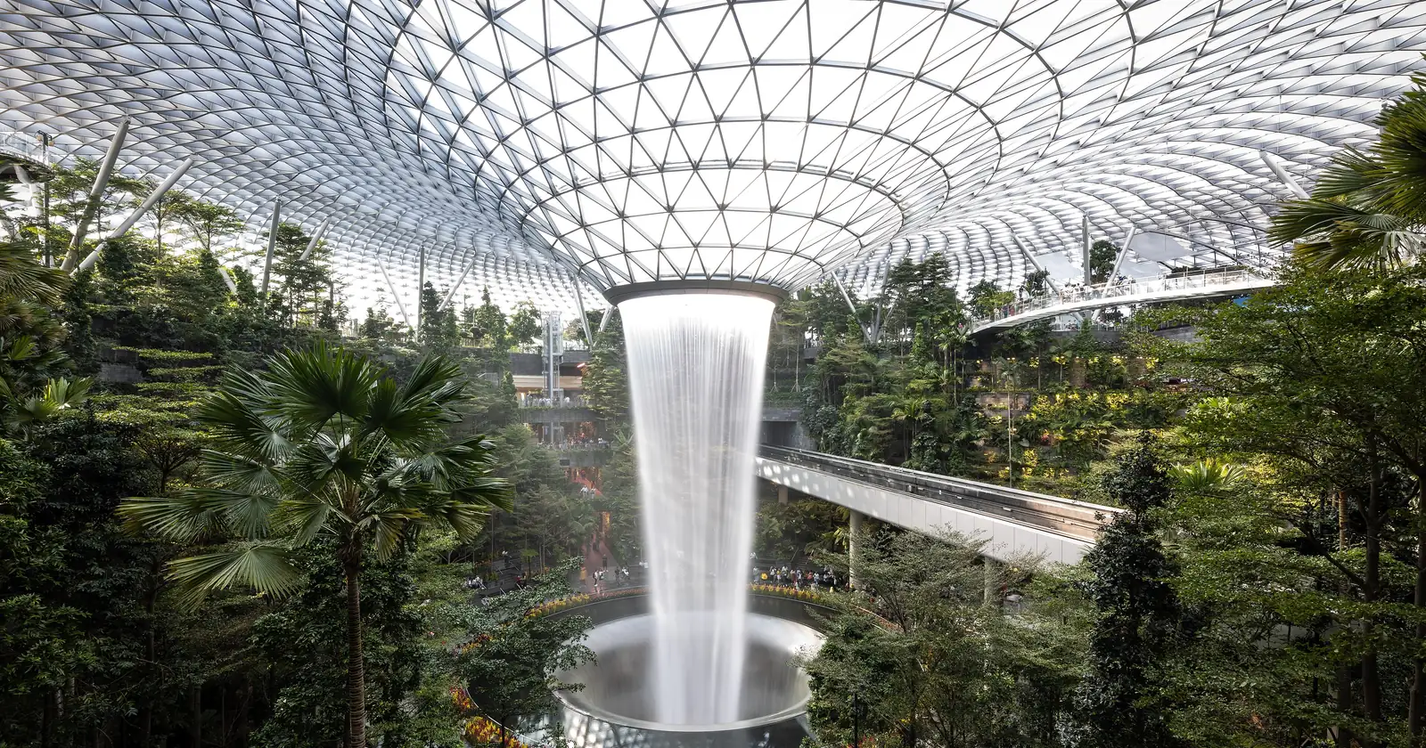 The Jewel Changi Airport Rain Vortex waterfall, falling through a glass-roofed atrium lined with tropical trees