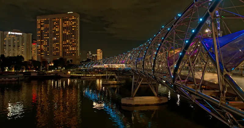 The Helix Bridge at night, its steel curves lit in blue and white beside the waterfront towers of Marina Bay