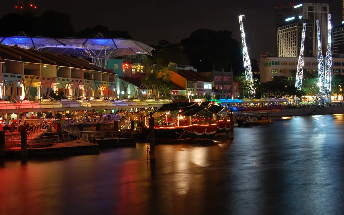 Clarke Quay on the Singapore River after dark, with lit riverside restaurants, moored boats and the water reflecting the lights