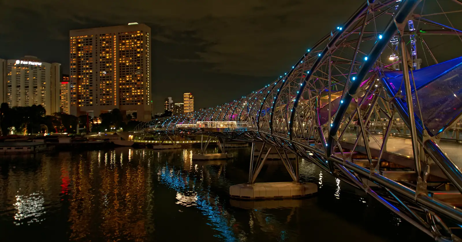 The Helix Bridge at night, its steel curves lit in blue and white beside the waterfront towers of Marina Bay