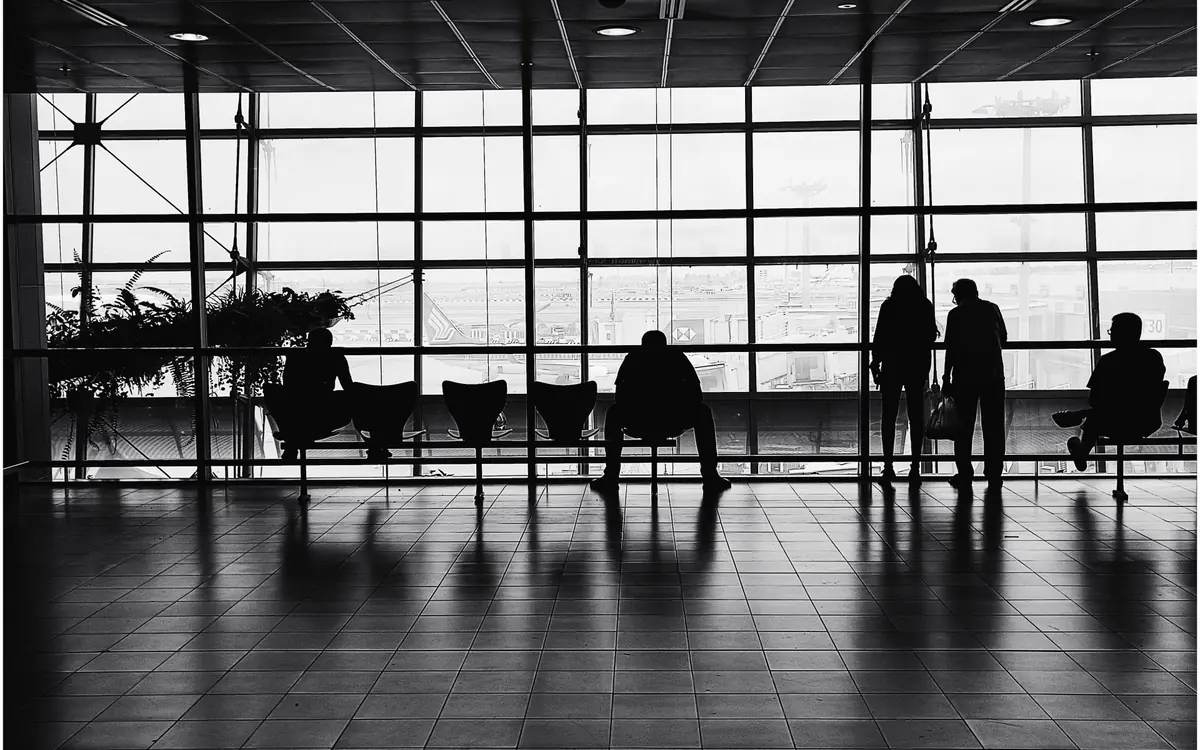 A waiting area inside Changi Airport Terminal 2 with silhouetted travellers seated beside a wall of windows